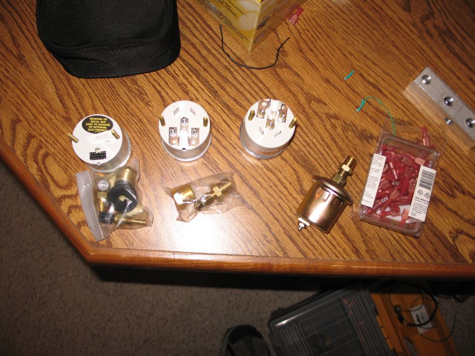 Aftermarket gauges, senders, brass fittings and wire connectors laid out on a wood table