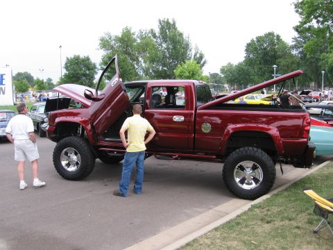 1989 Ford Mustang - A modified red pickup truck is displayed with its doors and hood open at an outdoor event.