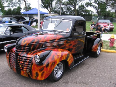 1989 Ford Mustang - A classic pickup truck with a custom flame paint job is displayed at an outdoor event.
