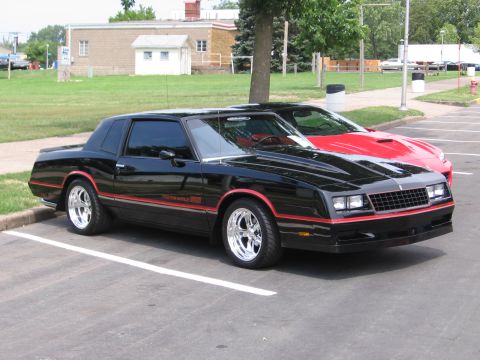 1989 Ford Mustang - A black 1981 Chevrolet Monte Carlo SS is parked next to a red car.