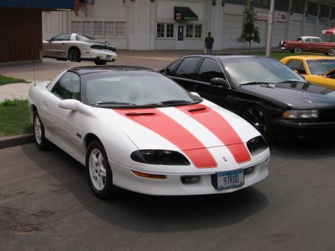 1989 Ford Mustang - A white Chevrolet Camaro Z28 with red racing stripes is parked in front of a building.