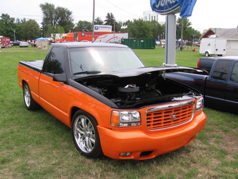 1989 Ford Mustang - A modified pickup truck with its hood open is displayed on a grassy field next to other vehicles.