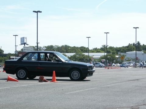 2001 Mercury Grand Marquis - A dark sedan navigates a course marked by orange cones in a parking lot, with other vehicles and spectators visible.