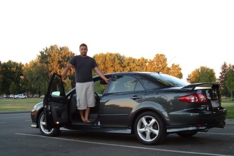 2005 Mazda 6 - Man stands by his 2005 Mazda 6 sedan, showing off the car's profile and spoiler.
