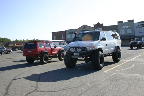 2003 Jeep TJ - A silver van and a red Jeep Cherokee, both heavily modified for off-road use, are parked in a lot.