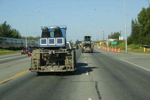 2003 Jeep TJ - A modified truck with tracks and a blue cabin is seen on the road, with a tractor in front and a train to the side.