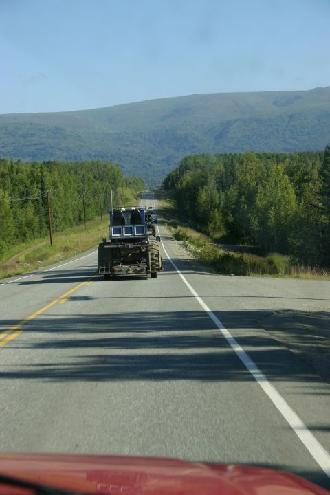 2003 Jeep TJ - A blue truck cab is transported on a trailer along a tree-lined highway under a clear blue sky.