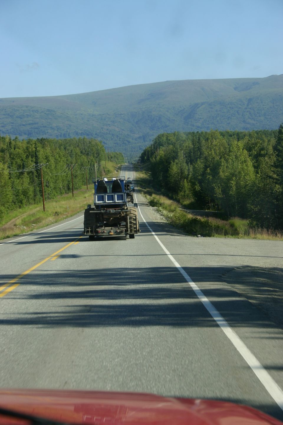 Blue truck cab on a flatbed trailer driving on a highway, seen from behind