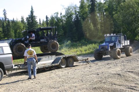 2003 Jeep TJ - Two large off-road vehicles are present, one being loaded onto a trailer by a man.