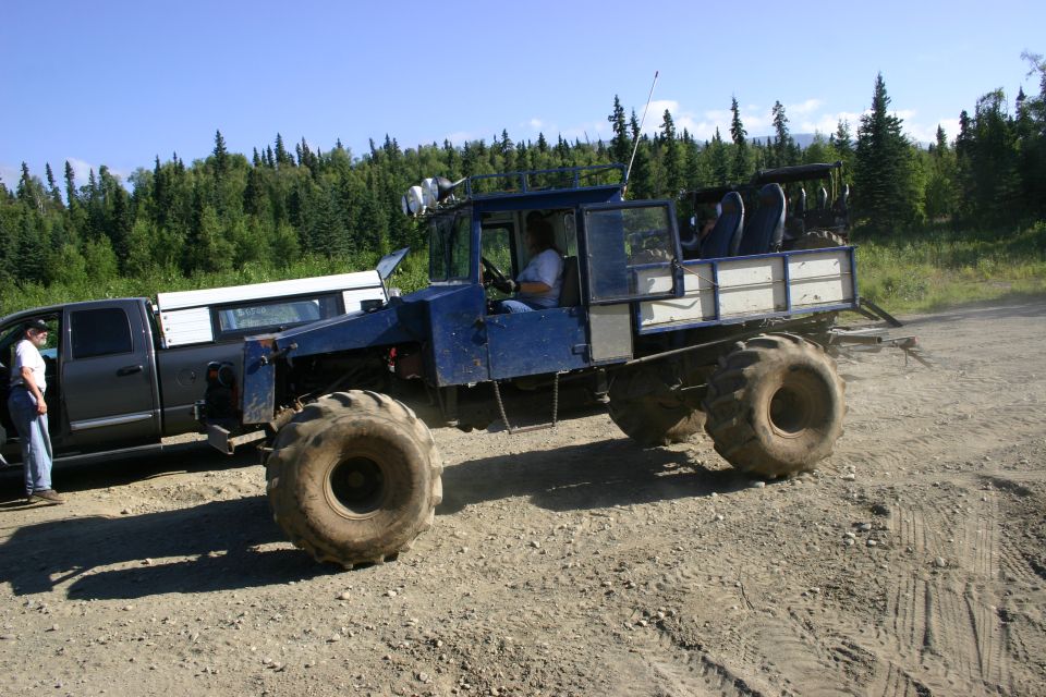 Blue custom off-road truck with large tires and a flatbed, parked next to a gray pickup truck