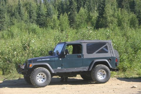 2003 Jeep TJ - A dark green Jeep Wrangler Unlimited is parked on a dirt road with a wooded background.