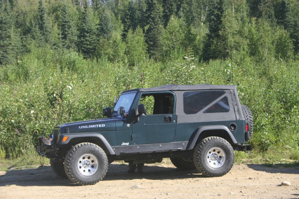 Dark green Jeep Wrangler Unlimited with a soft top, parked on a dirt road