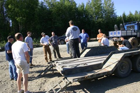 2003 Jeep TJ - A group of people stand around a trailer, with a large, custom blue vehicle visible in the background.