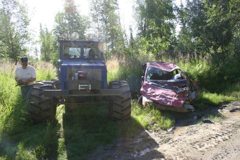 2003 Jeep TJ - A severely damaged red car sits on a dirt road, its front end crushed and windshield shattered.