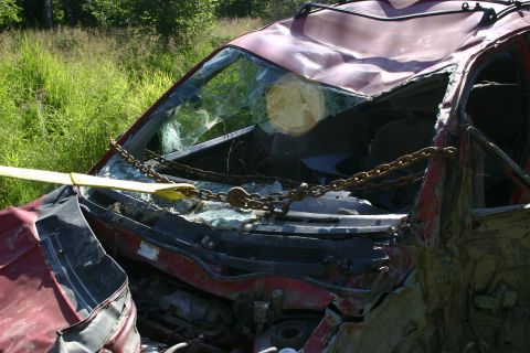 2003 Jeep TJ - A heavily damaged red vehicle is being towed, its windshield cracked and body severely crumpled.