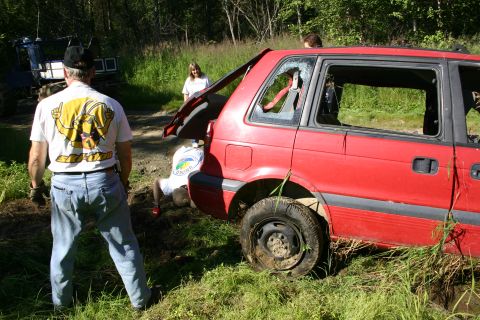 2003 Jeep TJ - A red SUV with damaged windows and an open tailgate sits in a grassy area with people nearby.