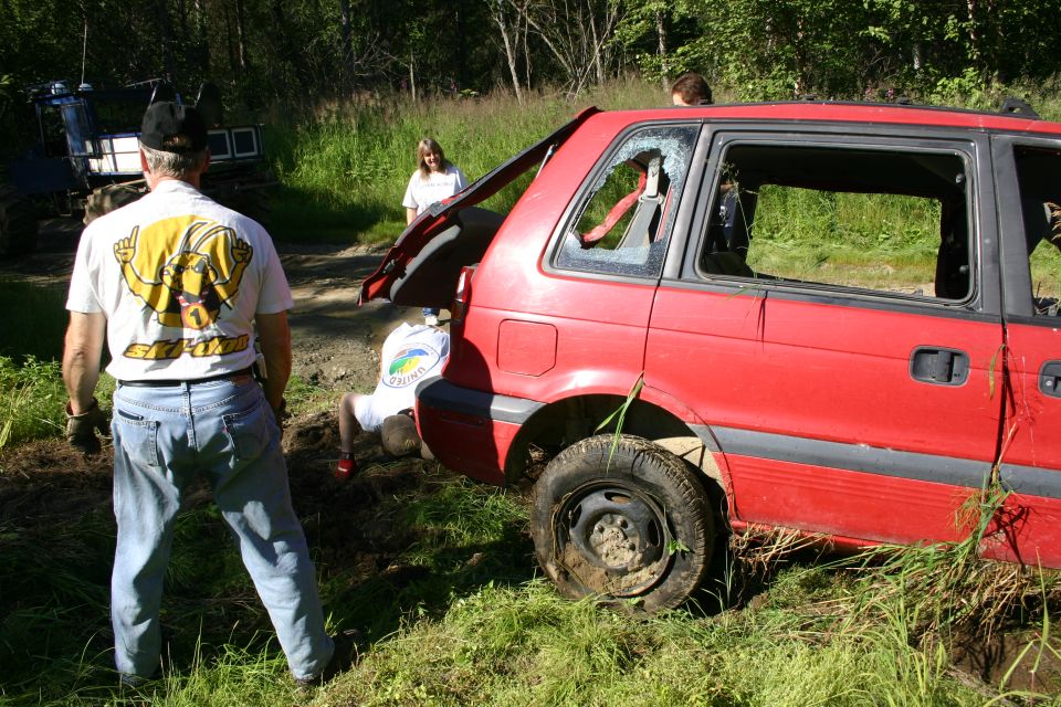 Side view of red SUV with broken windows and open tailgate, people around