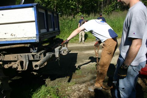 2003 Jeep TJ - Attaching a chain to a truck's hitch mechanism, with another vehicle's bed in view.