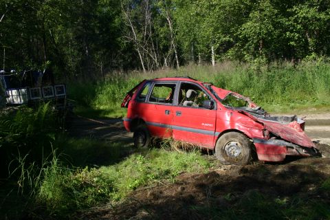 2003 Jeep TJ - A heavily damaged red minivan is being towed through a grassy area.