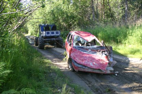 2003 Jeep TJ - A heavily damaged red car is being towed by a large, off-road vehicle on a dirt track.