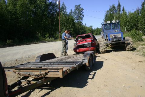 2003 Jeep TJ - A red car with a heavily damaged rear is being loaded onto a trailer, assisted by two individuals and a large blue all-terrain vehicle.