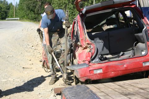 2003 Jeep TJ - A red SUV is being lifted by a jack on a dirt road, with two people attending to the vehicle.
