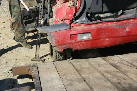 2003 Jeep TJ - A red vehicle is being lifted with a hi-lift jack onto a wooden surface.