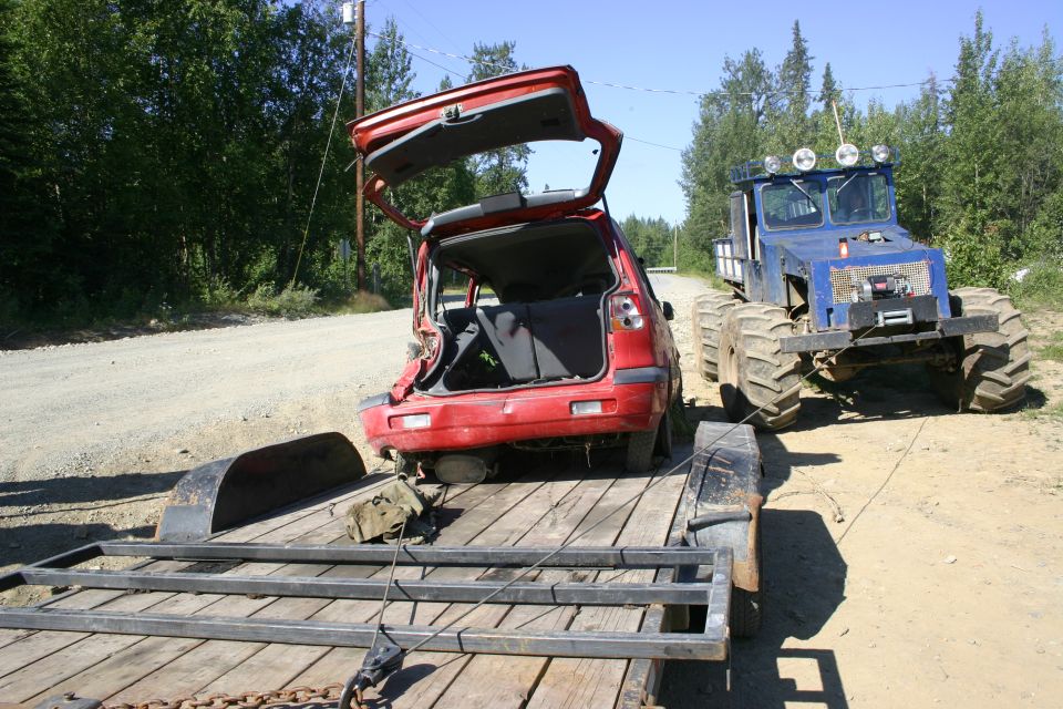 Red car on trailer towed by blue ATV with large tires