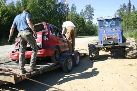 2003 Jeep TJ - A red SUV, appearing damaged, is being loaded onto a trailer with the assistance of a large blue tractor.