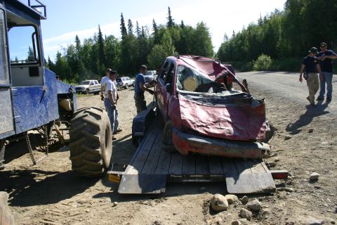 2003 Jeep TJ - A severely damaged red car is loaded onto a trailer, with a large blue tractor unit nearby.