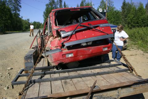2003 Jeep TJ - This heavily damaged red SUV is being transported on a trailer, with a person standing nearby.