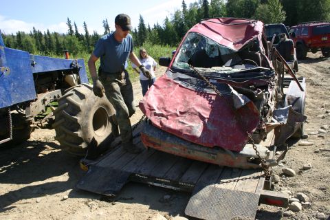 2003 Jeep TJ - A severely damaged red SUV is being winched onto a trailer, with a blue tractor assisting the recovery effort.