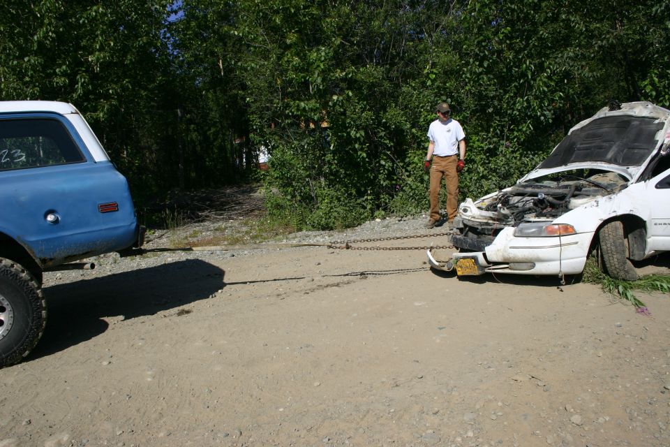 White sedan with hood open, chained to blue SUV, with a person standing nearby
