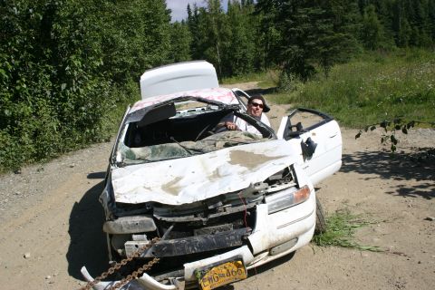 2003 Jeep TJ - A severely damaged white sedan sits on a dirt road with a person in the driver's seat.