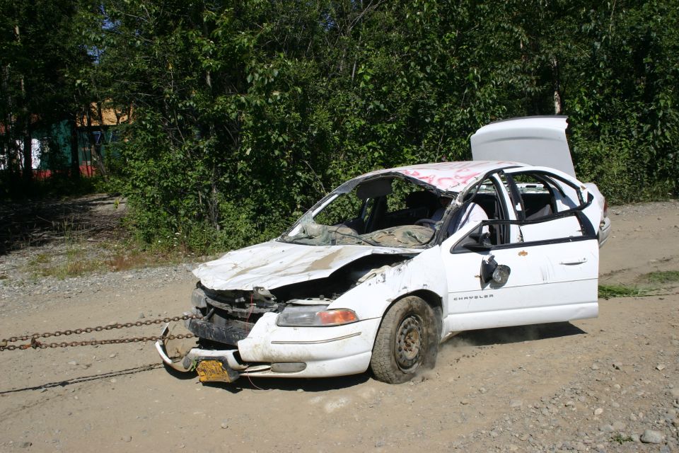 Damaged white sedan with open trunk and door, pulled by chains