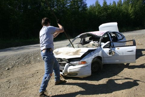 2003 Jeep TJ - A damaged white sedan sits on a dirt road with its doors ajar as a person prepares to strike it with a pole.