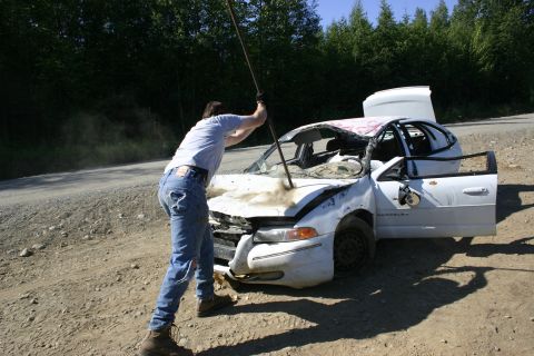 2003 Jeep TJ - A person uses a pole on the hood of a heavily damaged white sedan with its roof caved in and doors open.