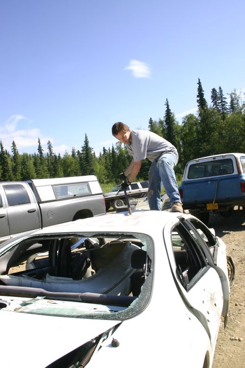 2003 Jeep TJ - A person stands on the roof of a damaged white car, with other vehicles in a junkyard setting.