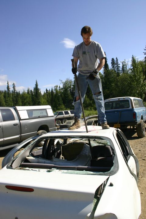 2003 Jeep TJ - Man on top of a wrecked car, with other vehicles nearby under a blue sky.