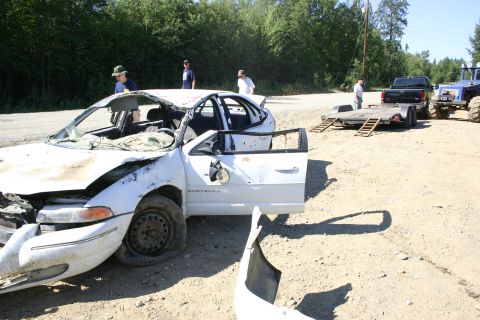 2003 Jeep TJ - A heavily damaged white sedan sits on a dirt lot with its doors ajar and a detached bumper nearby, while other vehicles and a trailer are v…