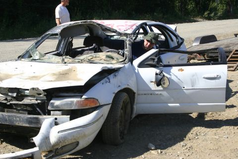 2003 Jeep TJ - A heavily damaged white sedan sits outdoors with its driver's side door ajar and a person visible inside.