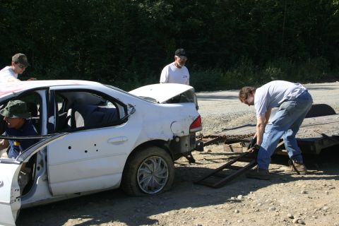 2003 Jeep TJ - A white sedan, appearing damaged, is being winched onto a trailer by a person in blue jeans.