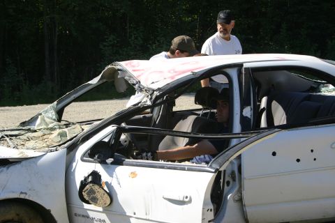 2003 Jeep TJ - A severely damaged white sedan sits outdoors with its roof compromised and bullet holes visible.