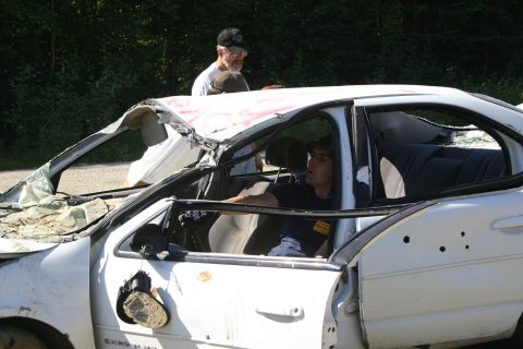 2003 Jeep TJ - A severely damaged white sedan sits outdoors with two individuals near or inside the vehicle.