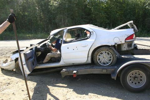 2003 Jeep TJ - A white sedan, heavily damaged and missing parts, is loaded onto a trailer for transport.