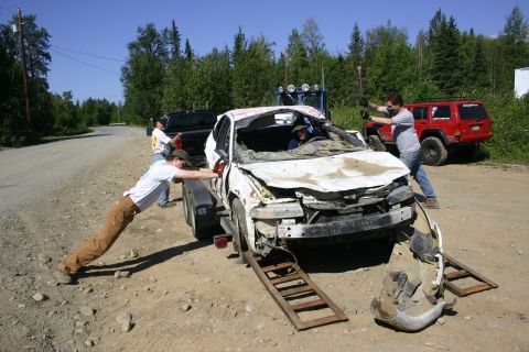 2003 Jeep TJ - A severely damaged car is being winched onto a trailer by several people, with other vehicles present.