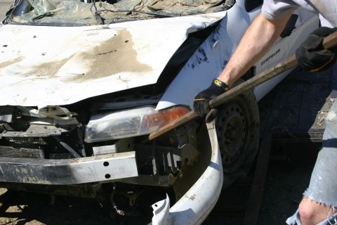 2003 Jeep TJ - A person in work gloves uses a metal bar to manipulate the damaged front end of a white car.