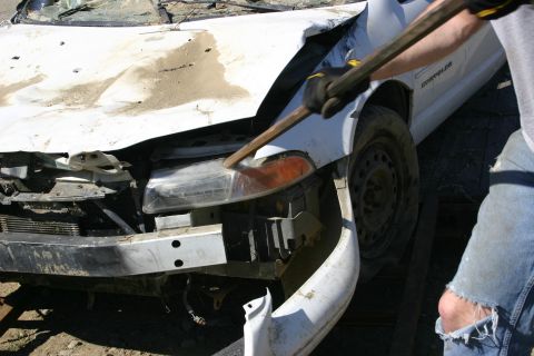 2003 Jeep TJ - A person is shown hitting the damaged front end of a white car with a stick.