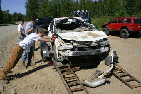 2003 Jeep TJ - A severely damaged white sedan is being winched onto a trailer by several individuals.