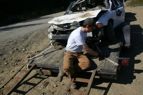 2003 Jeep TJ - A person secures a heavily damaged white car onto a trailer.